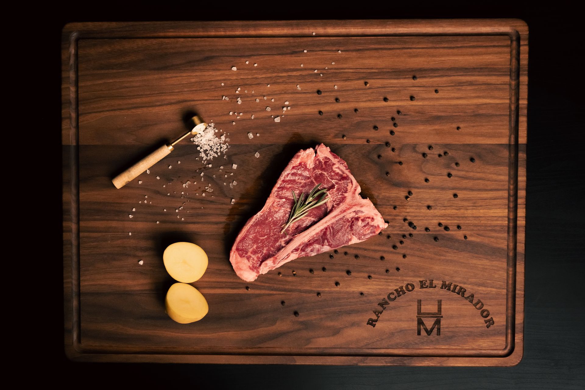 A piece of raw meat is sitting on a wooden table next to potatoes.