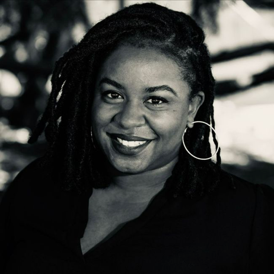 A woman with dreadlocks and hoop earrings is smiling in a black and white photo.