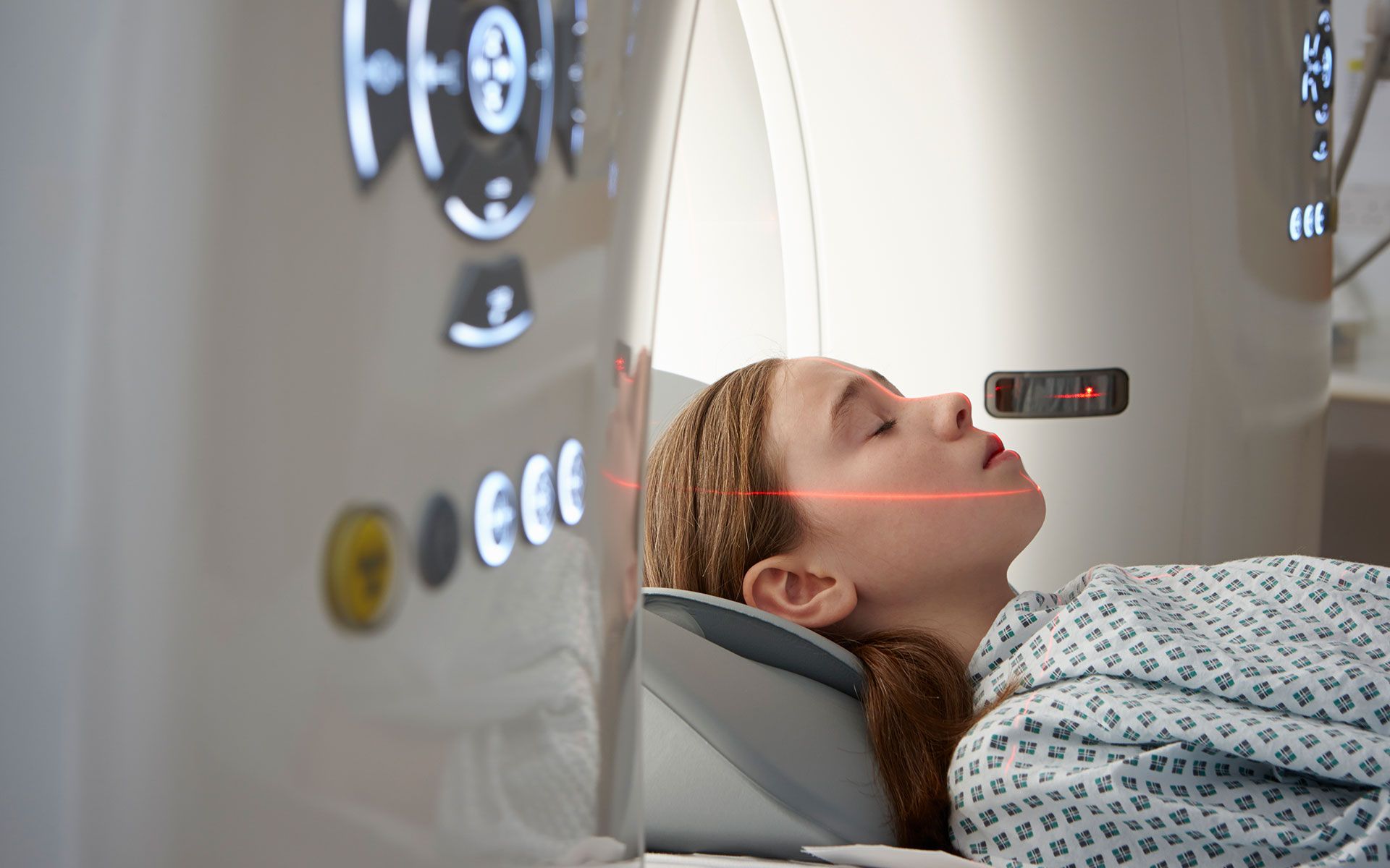 Young person undergoing a medical scan, lying down with a laser pointed at their face.