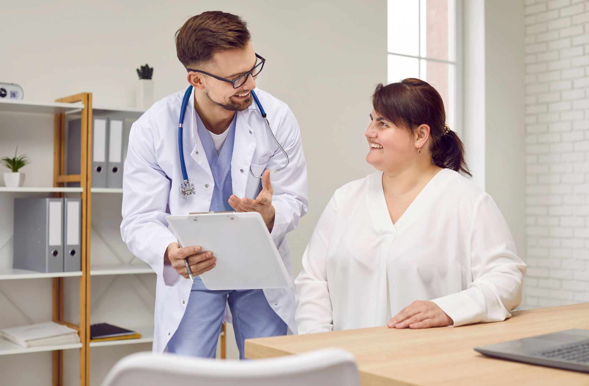 Doctor reviewing a clipboard with a seated patient in a bright clinic office