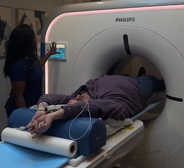Person undergoing a CT scan in a medical setting, with a healthcare worker operating the machine.