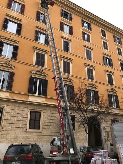 Davanti a un grande edificio è parcheggiato un camion con attaccata una scala.