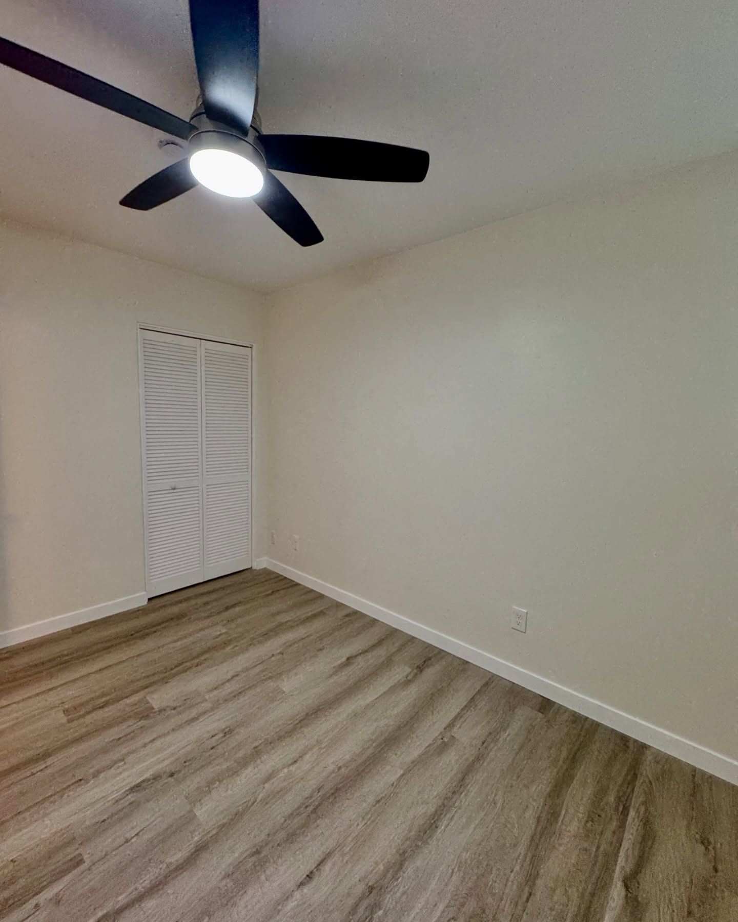 Bedroom with light wooden floor, white walls, closet, and ceiling fan.
