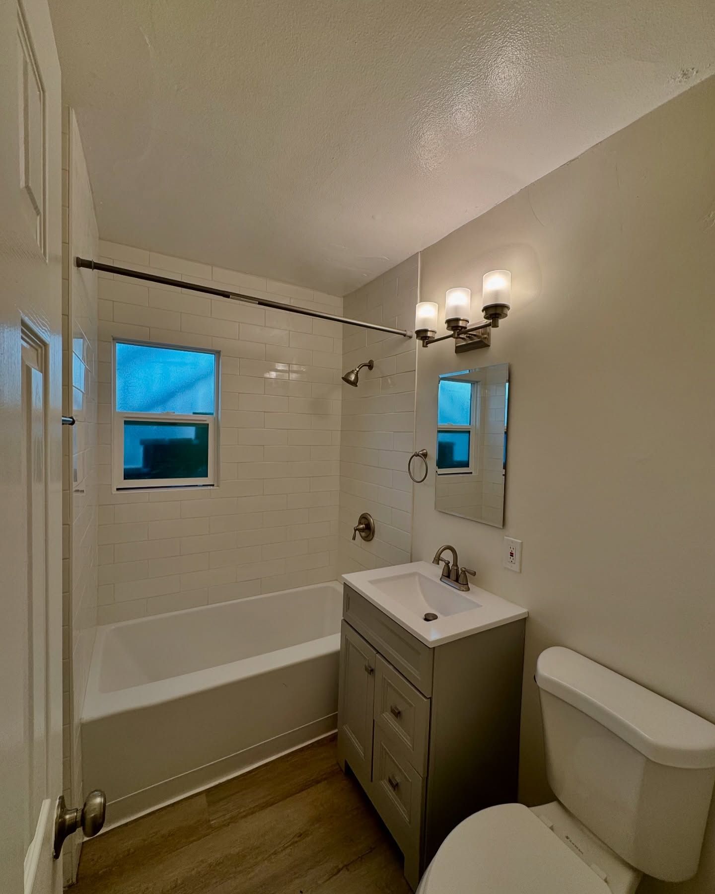 Bathroom with white tile shower, vanity, and toilet. Light gray walls and flooring.