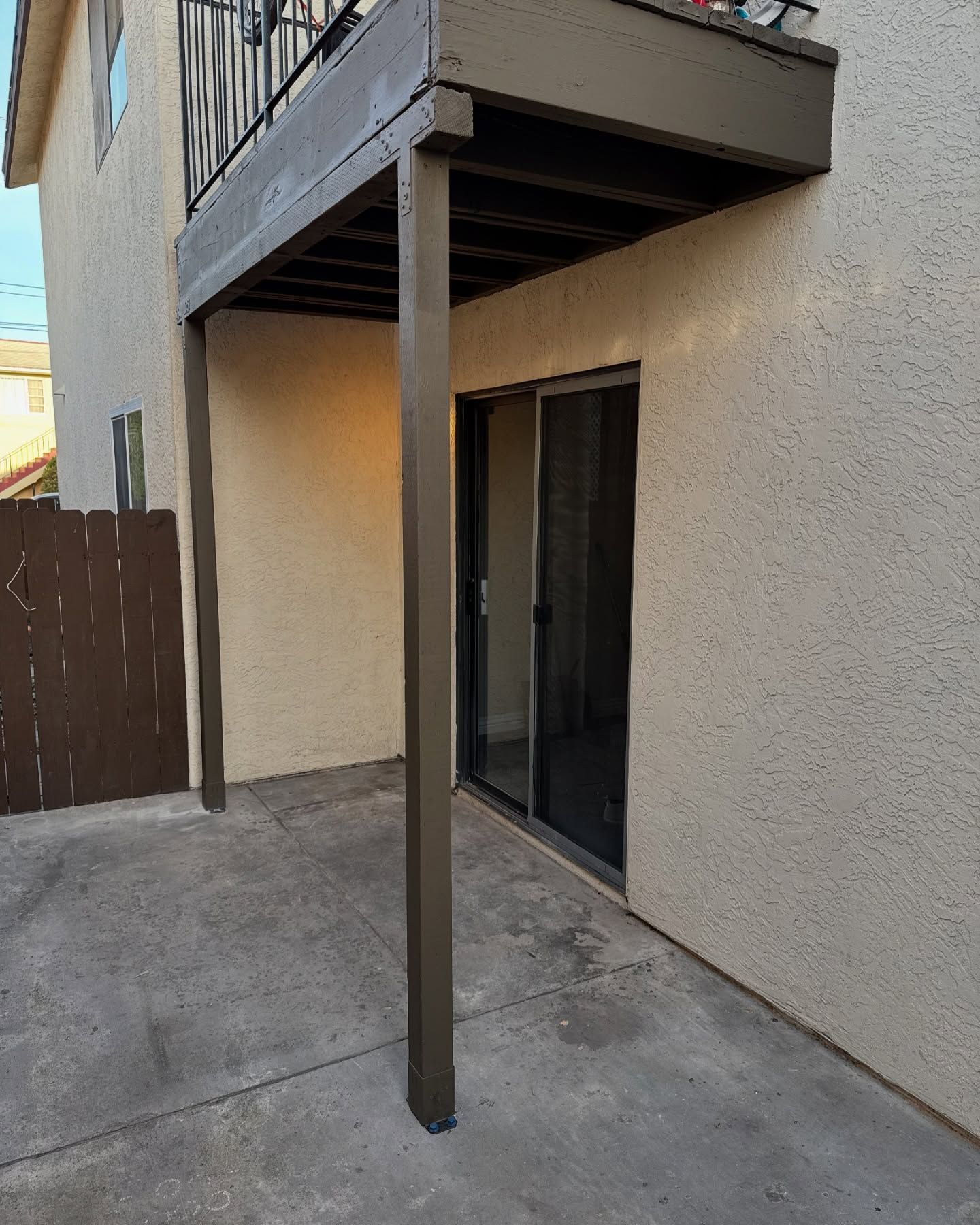 Back patio with brown deck above sliding glass door. Concrete ground, beige stucco walls.