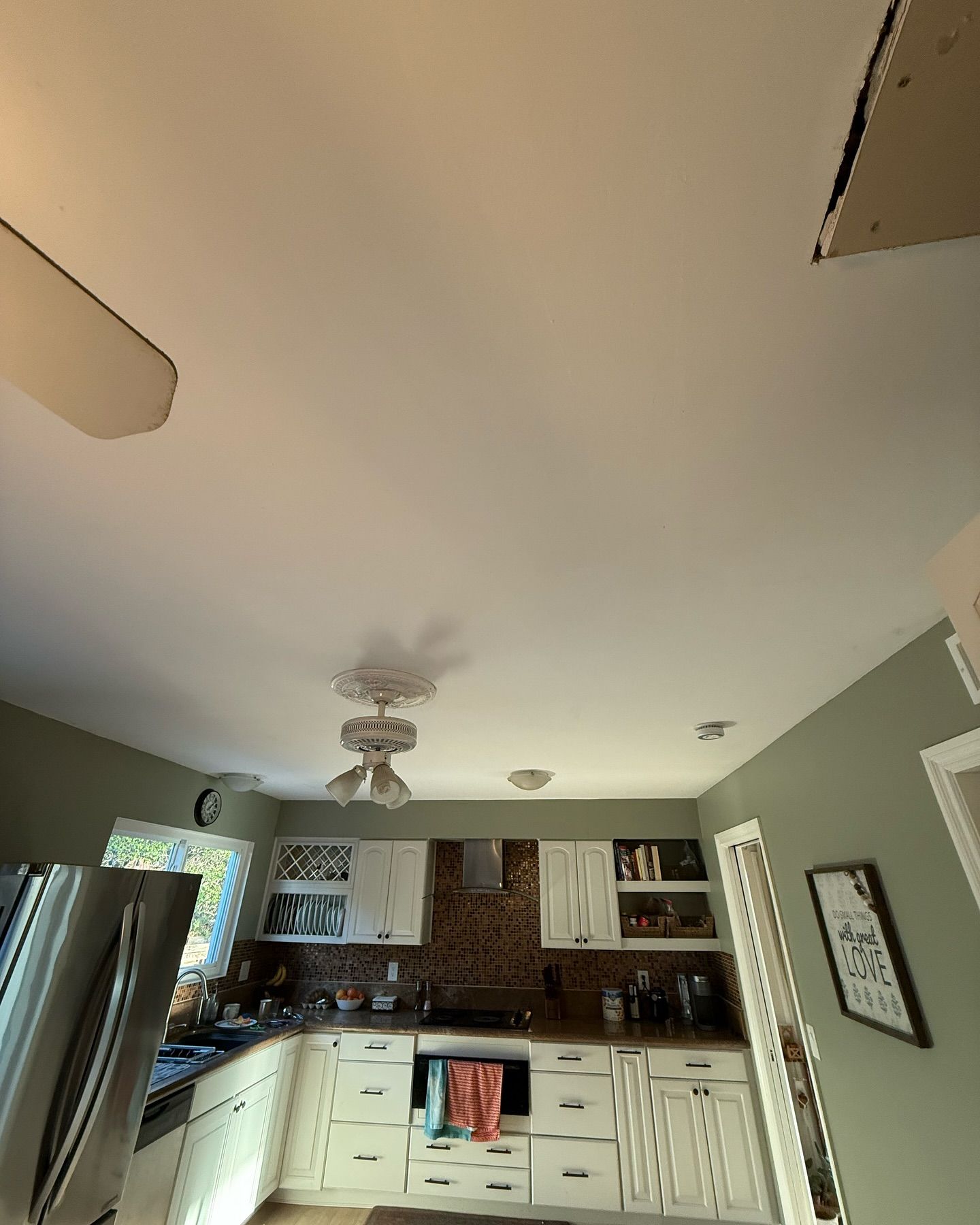 Kitchen ceiling with water damage and exposed drywall. White cabinets, appliances, and sage green walls.