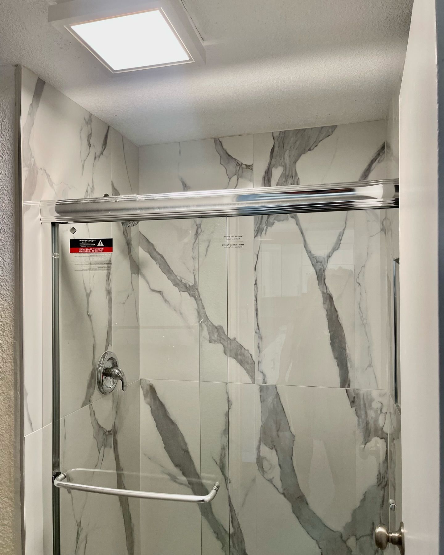 Shower with marble-look tile walls, chrome fixtures, and a glass sliding door.