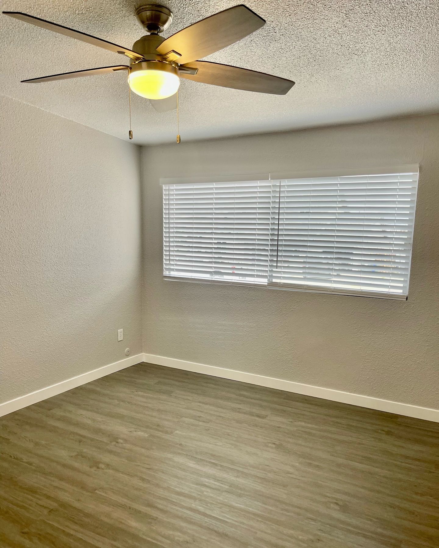 Empty room with ceiling fan, window with blinds, and wood-look flooring.