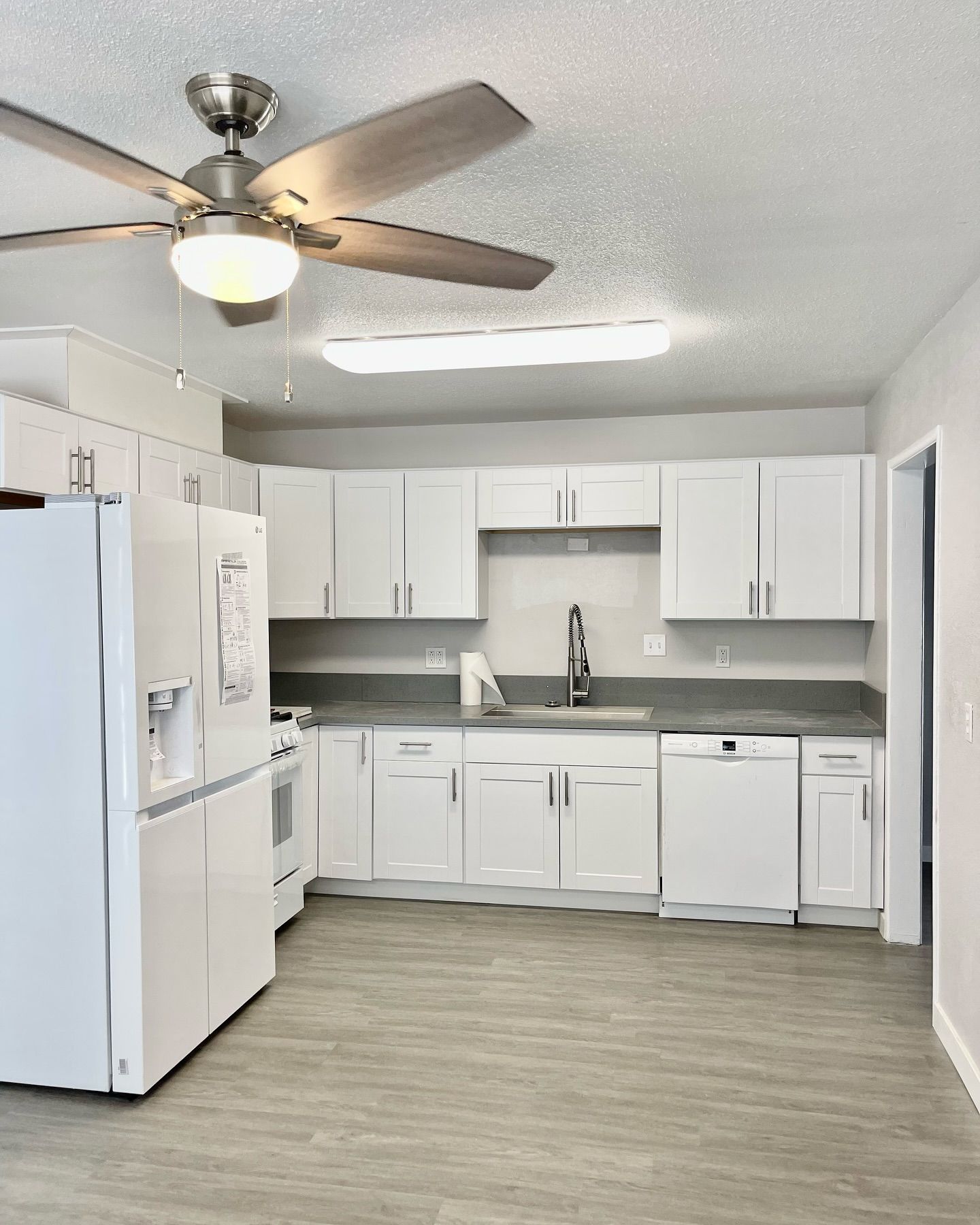 White kitchen with white cabinets, appliances, gray countertops, and wood-look flooring.