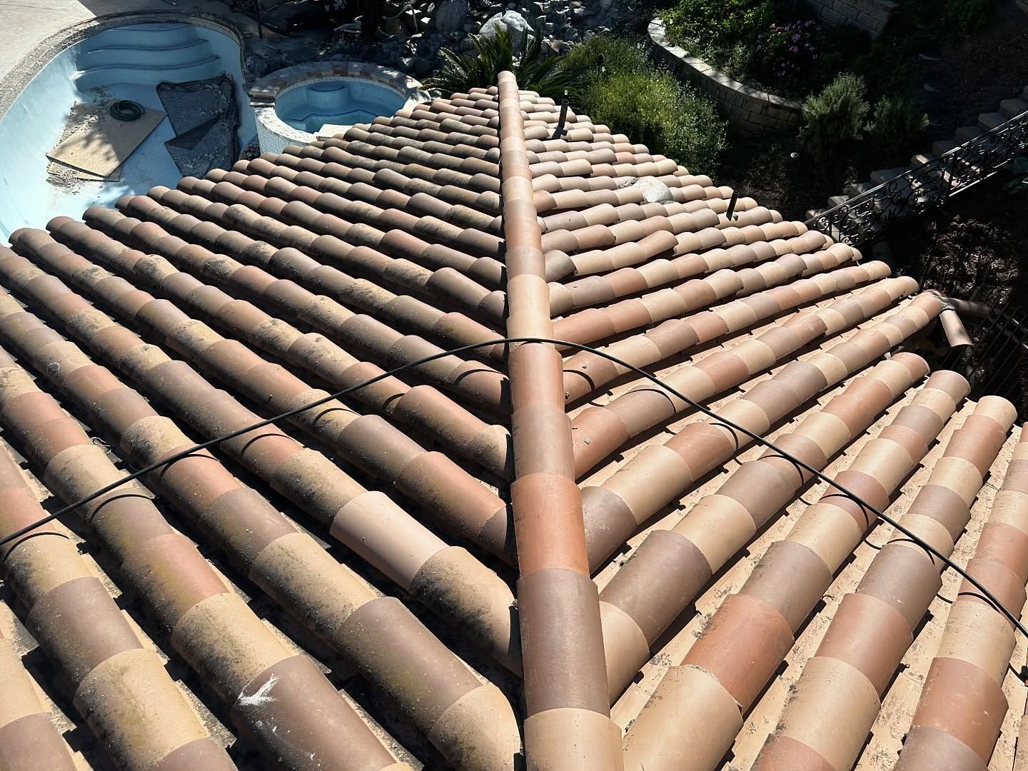 Clay tile roof with ridge cap, view from above. A pool and vegetation are visible in the background.