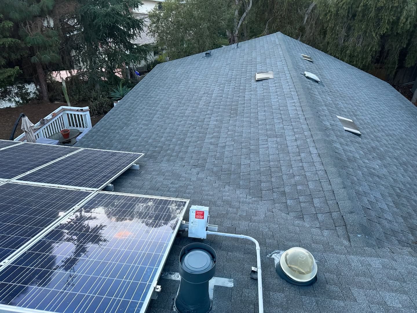Rooftop with solar panels and asphalt shingles. Chimney and vent pipes visible.