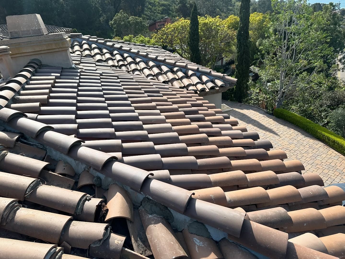 Clay tile roof with varying shades of brown. Rooftop view with trees and gravel.