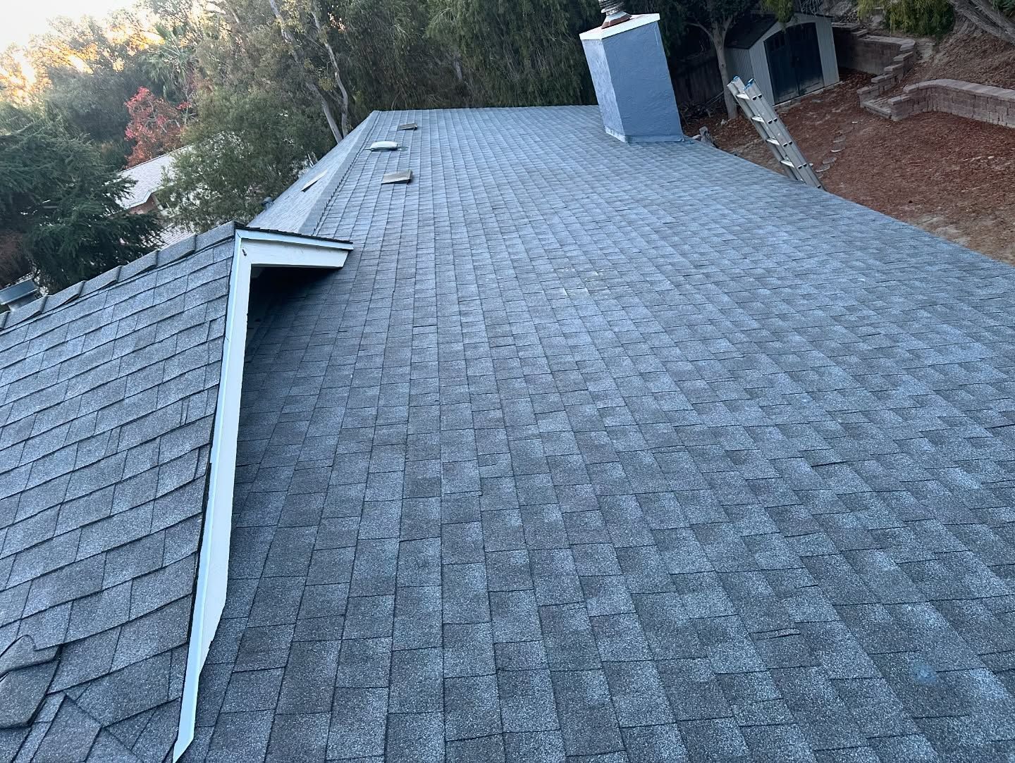 Gray shingled roof with a chimney, viewed from a high angle outdoors on a sunny day.