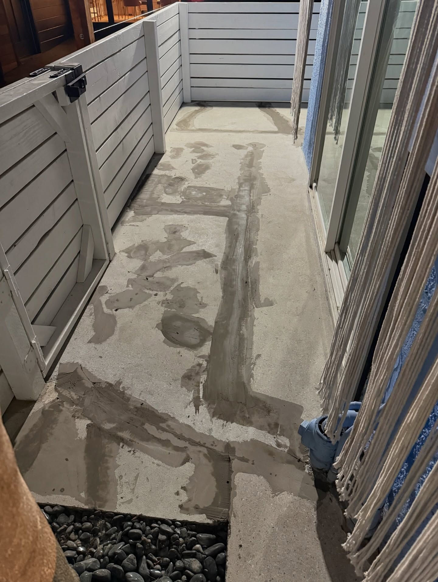Concrete pathway with repairs, leading to white fence gate. Black pebbles are in a border.