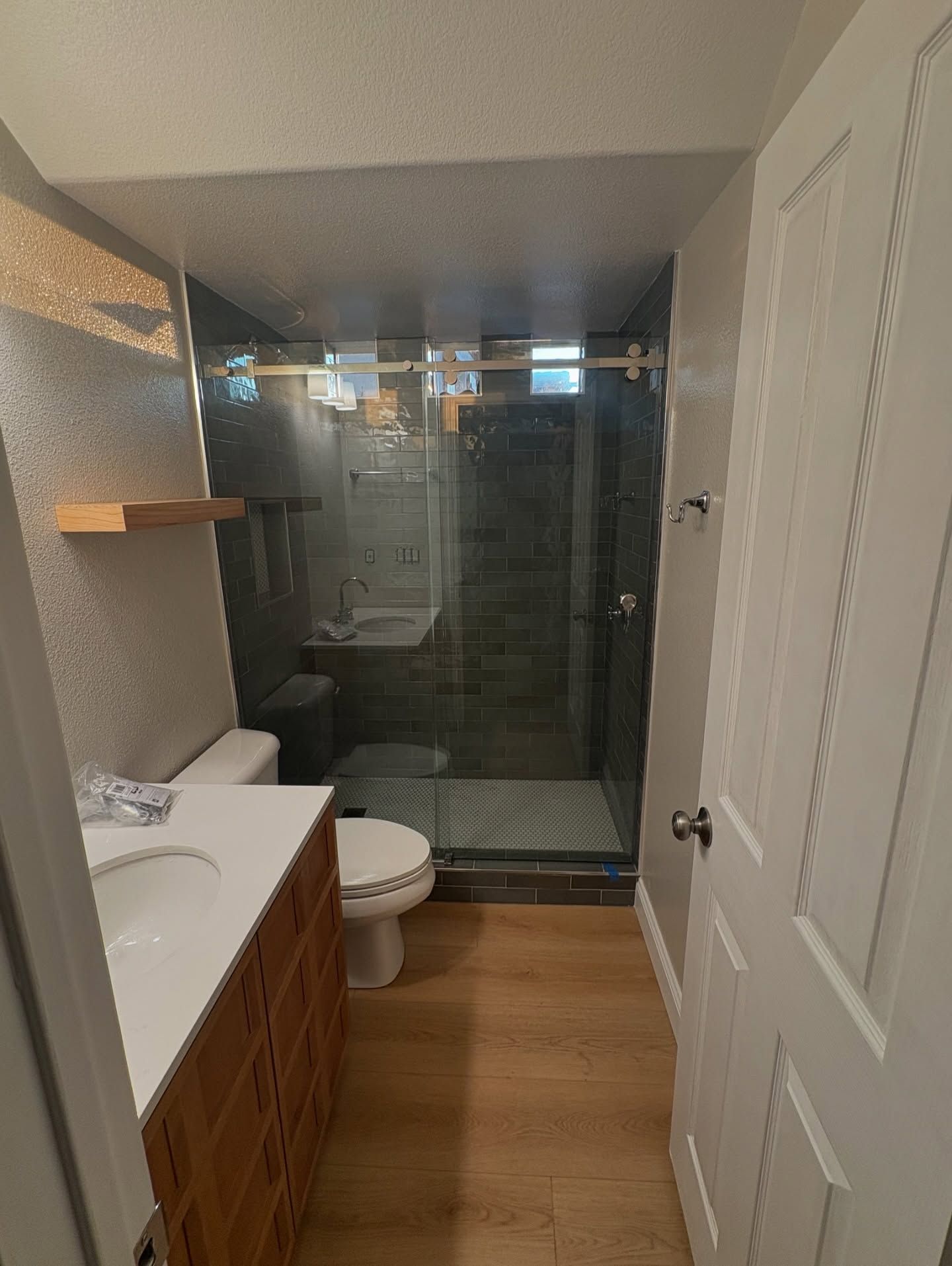 Bathroom with wood vanity, toilet, glass shower, and light wood flooring.
