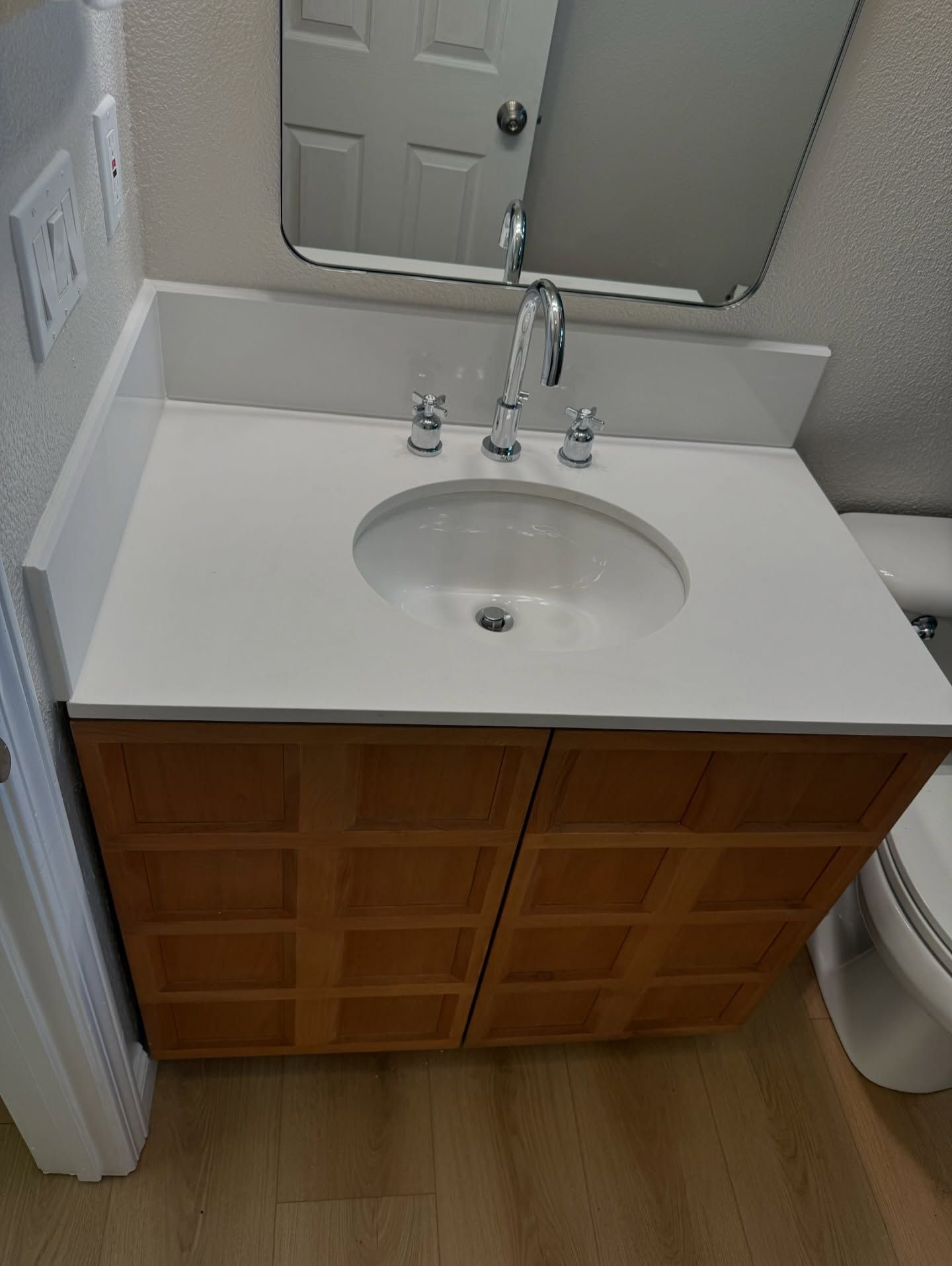 Bathroom vanity with white countertop, oval sink, and wood cabinet. A chrome faucet and mirror are above.