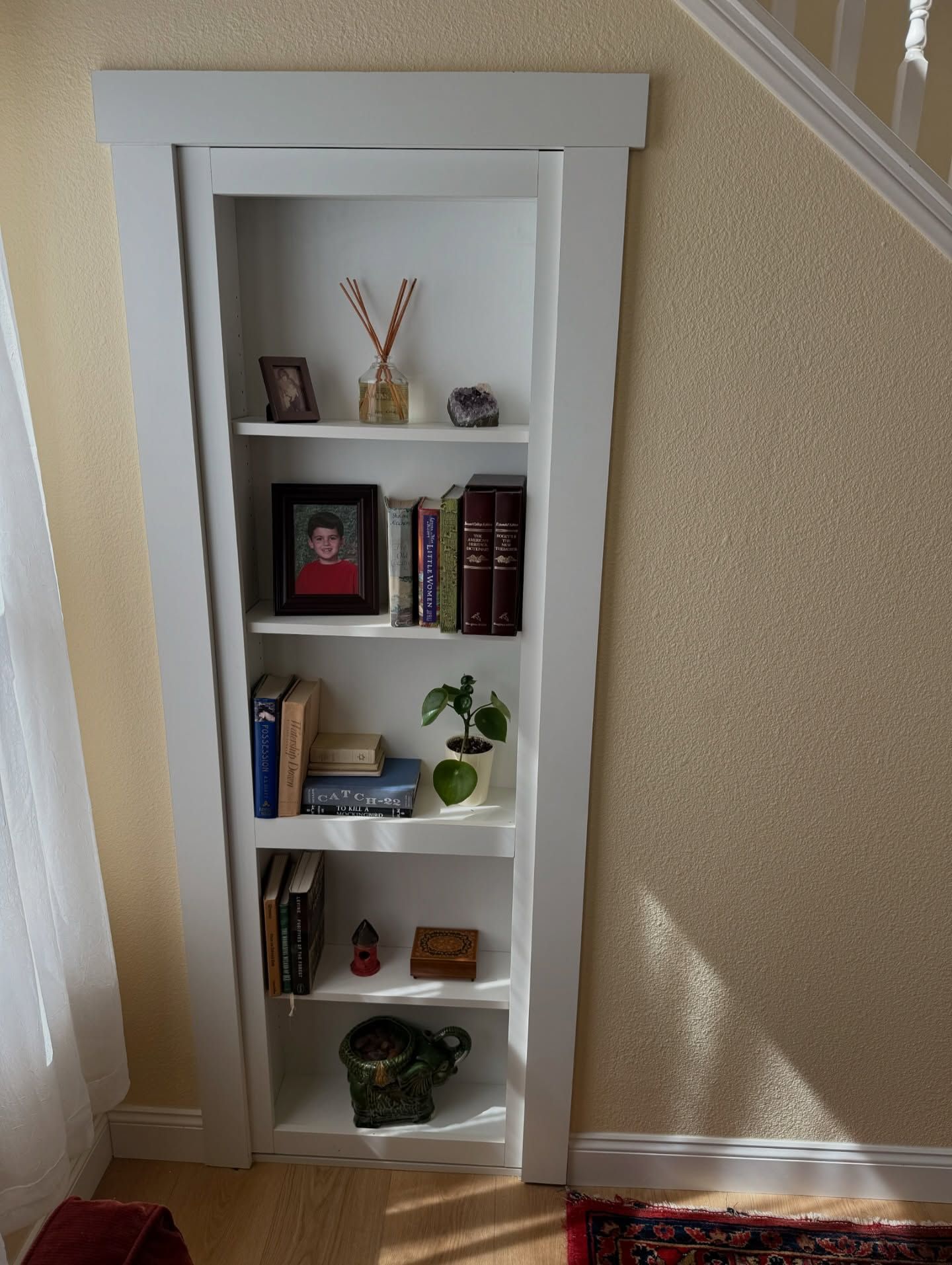 White-framed built-in bookshelf in a wall niche, filled with books, photos, and decorative items.