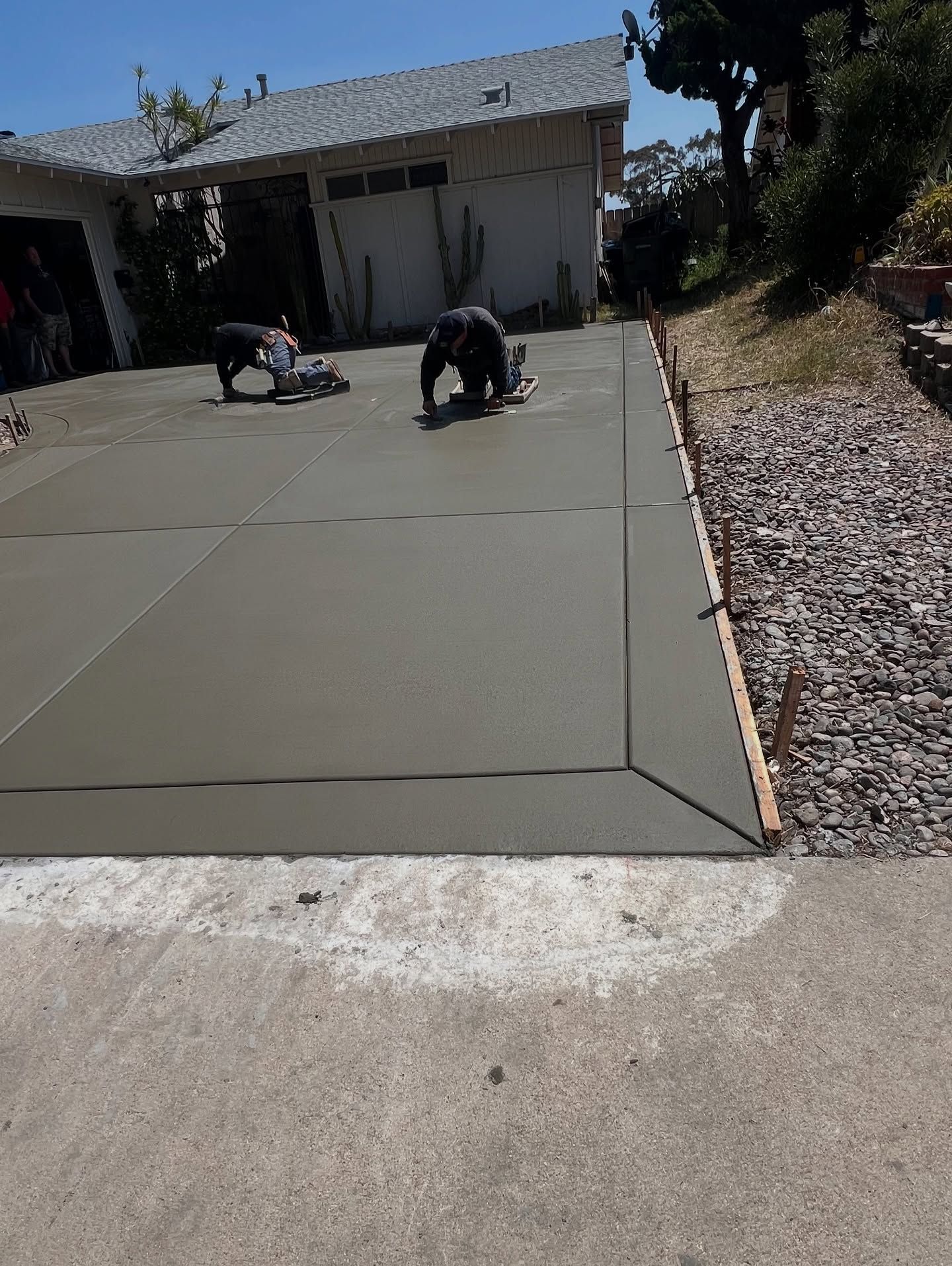 Two workers smoothing fresh concrete driveway with garage in the background.