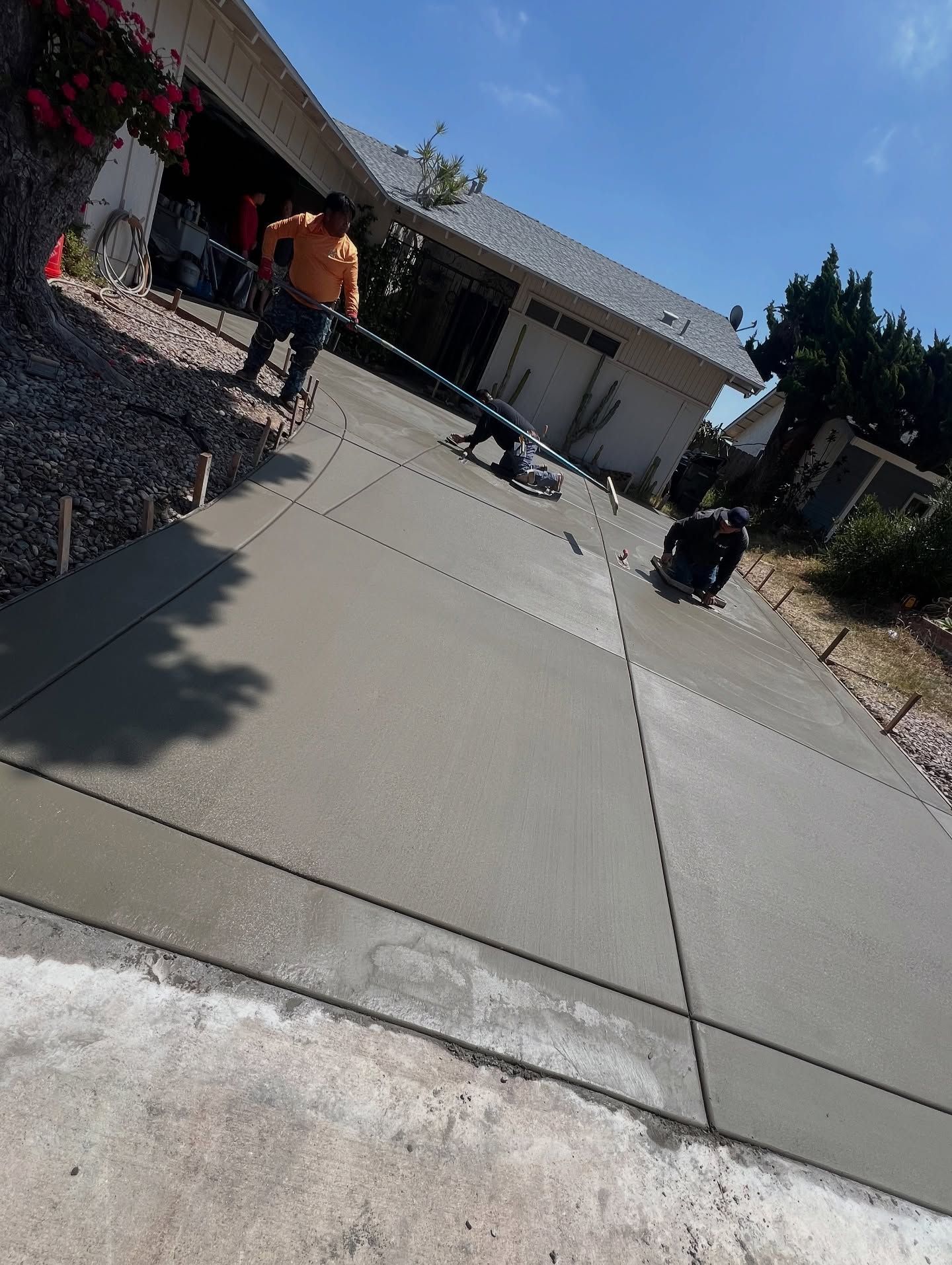 Workers leveling wet concrete on a driveway on a sunny day.