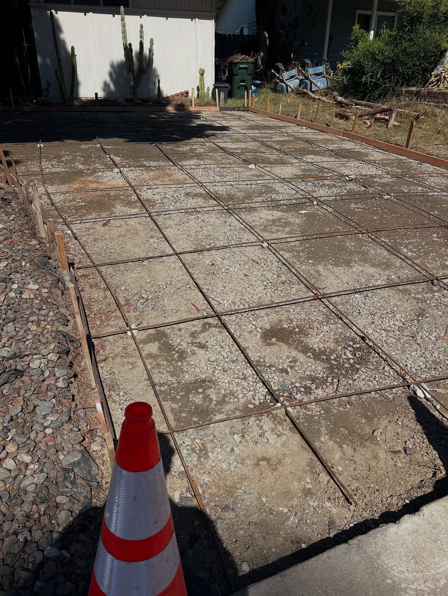 Driveway under construction with exposed rebar grid and traffic cone.