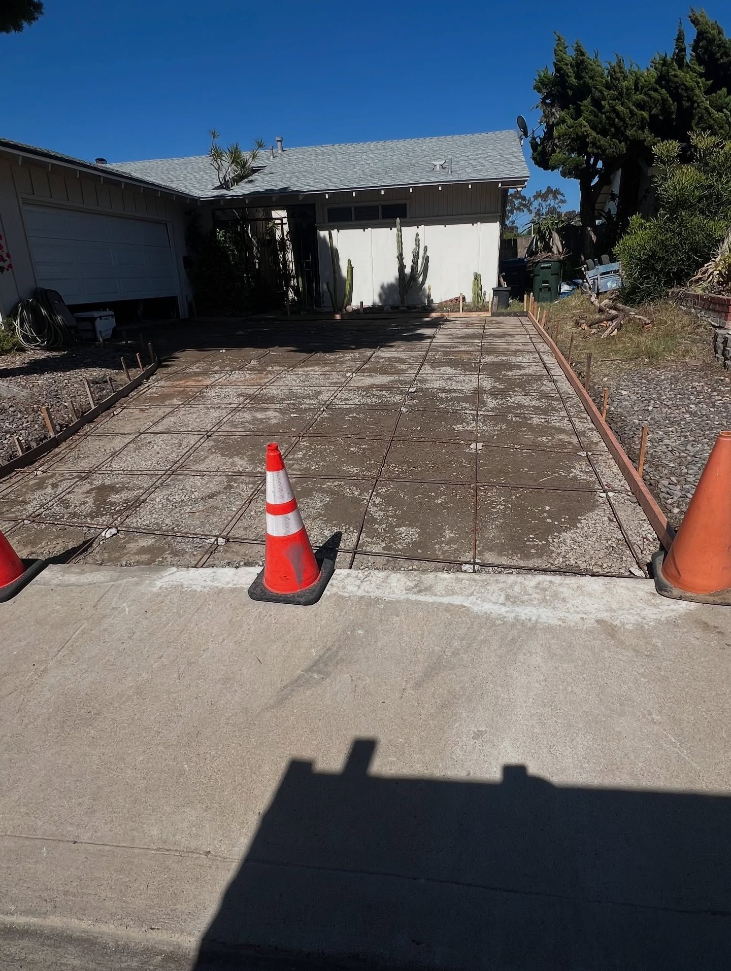 Driveway under construction with orange cones, leading to a house under a clear sky.