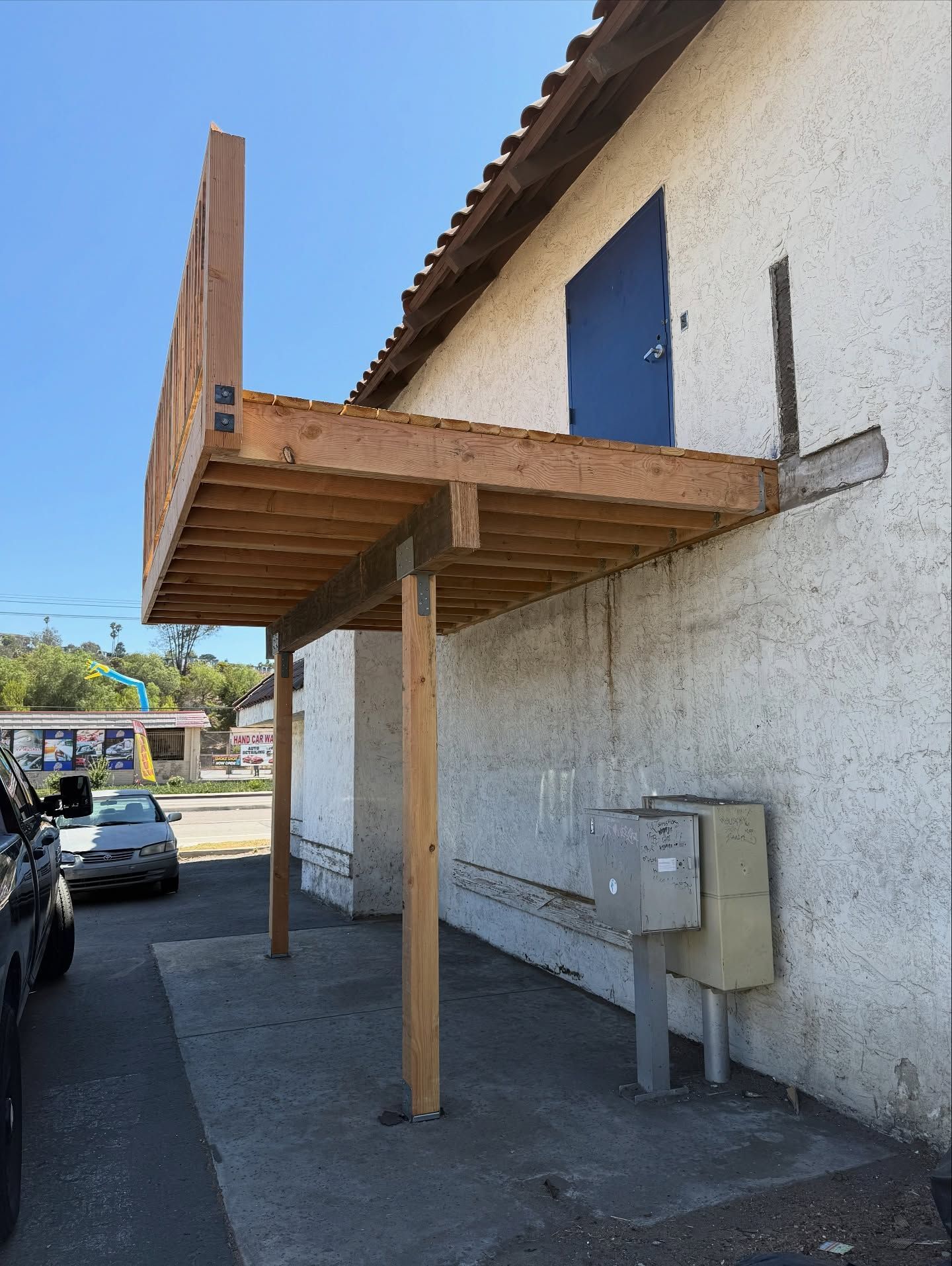 Wooden deck attached to a building's side, supported by posts. A blue door is visible on the building.