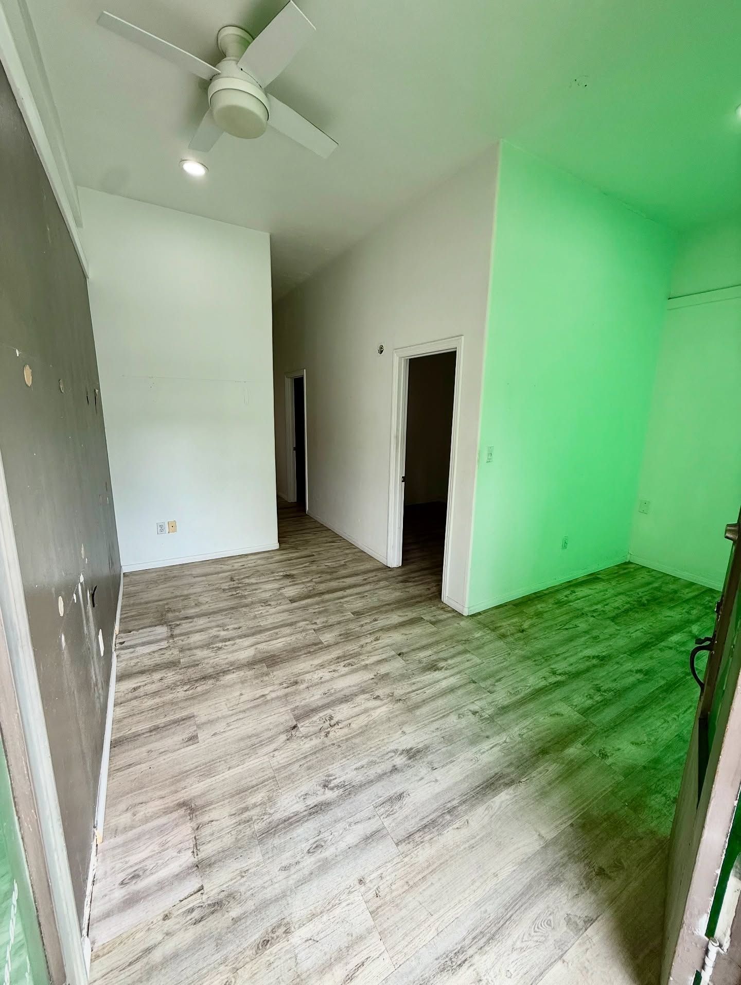 Empty room with light-colored wood flooring, white and green walls, and an open doorway leading to a hallway.