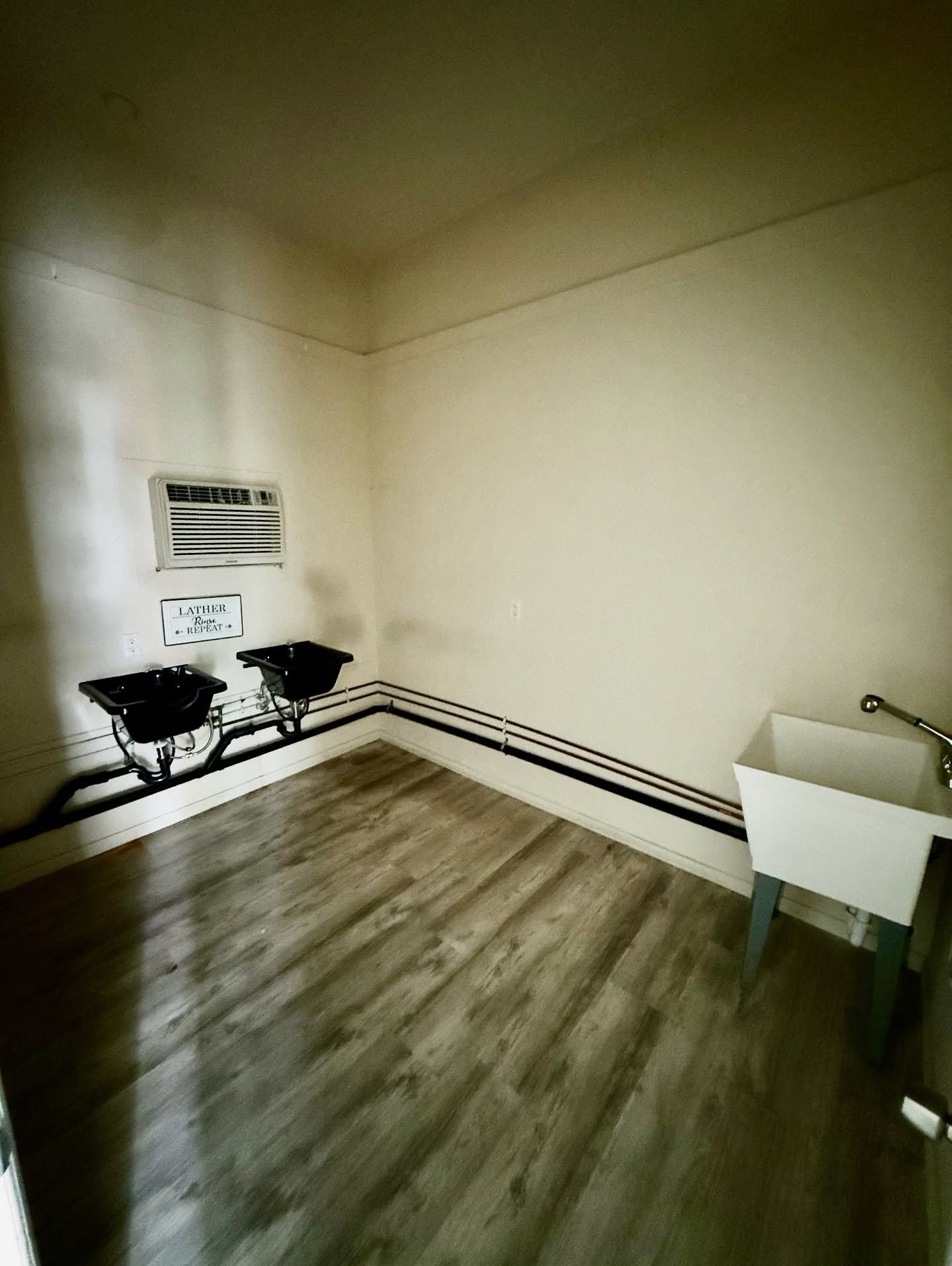 Laundry room with two black sinks, white utility sink, and wood-look flooring. Air conditioner visible.