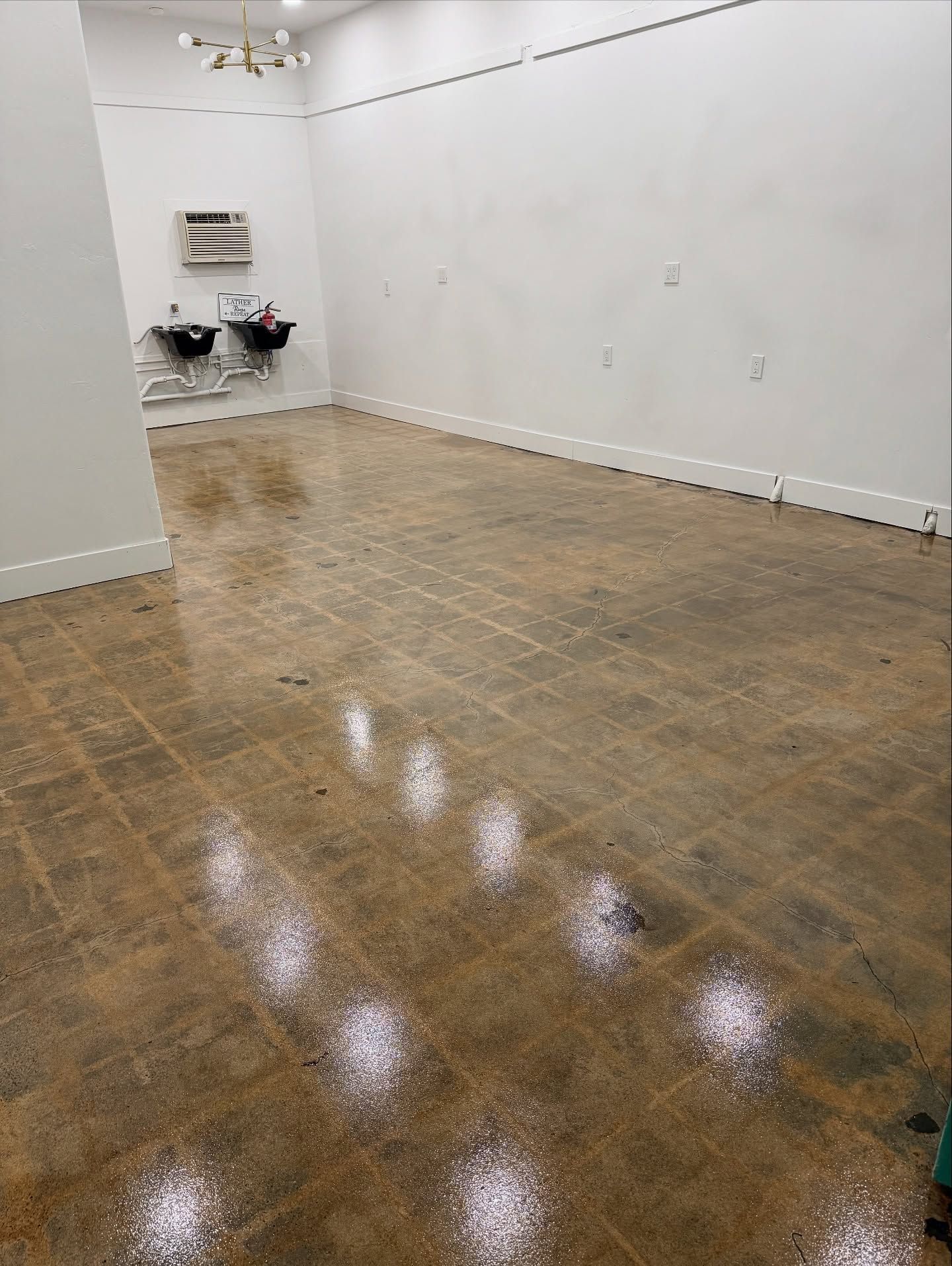 Empty room with glossy brown floor, white walls. Two sinks visible in the back.