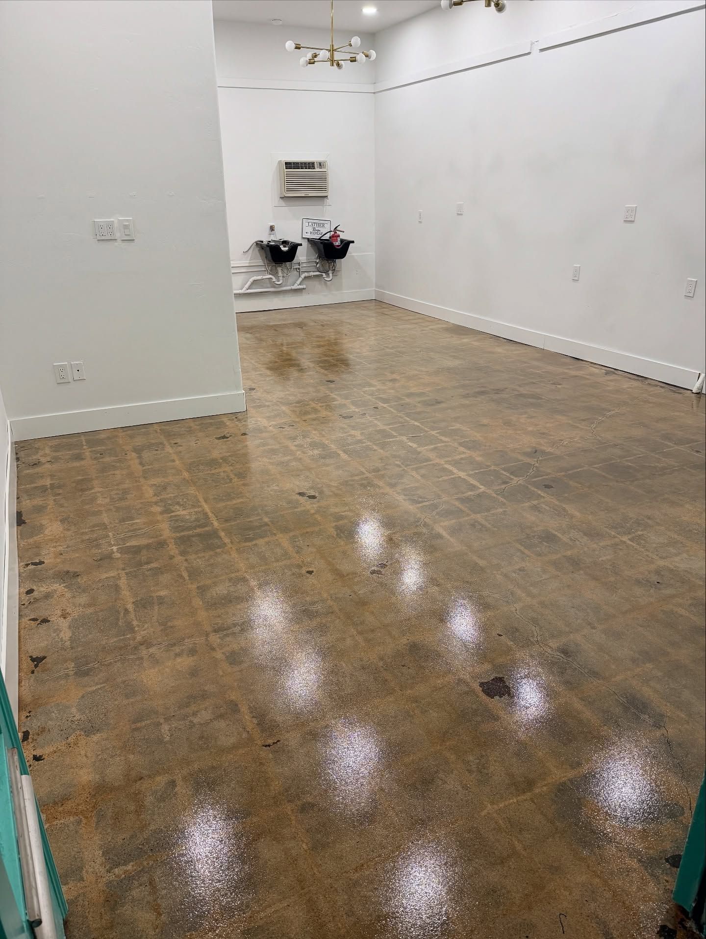 Empty room with polished concrete floor and white walls; sinks in the back.