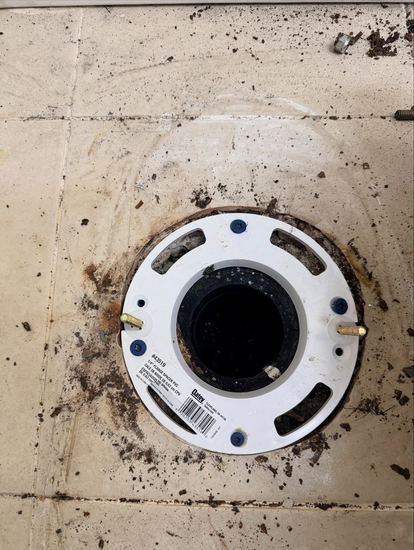 White toilet flange on dirty tiled floor, with mounting bolts.