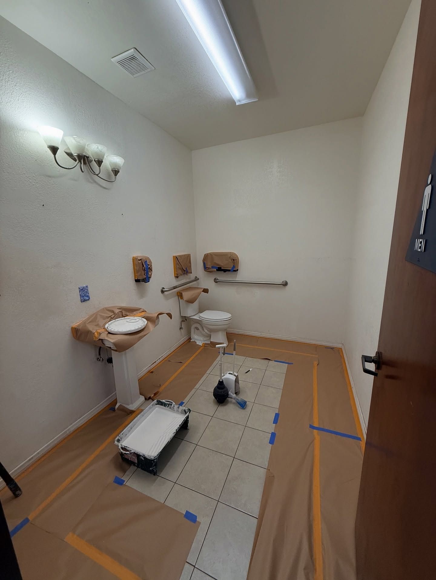 Interior of an accessible restroom with protective coverings on the floor and fixtures, ready for painting.