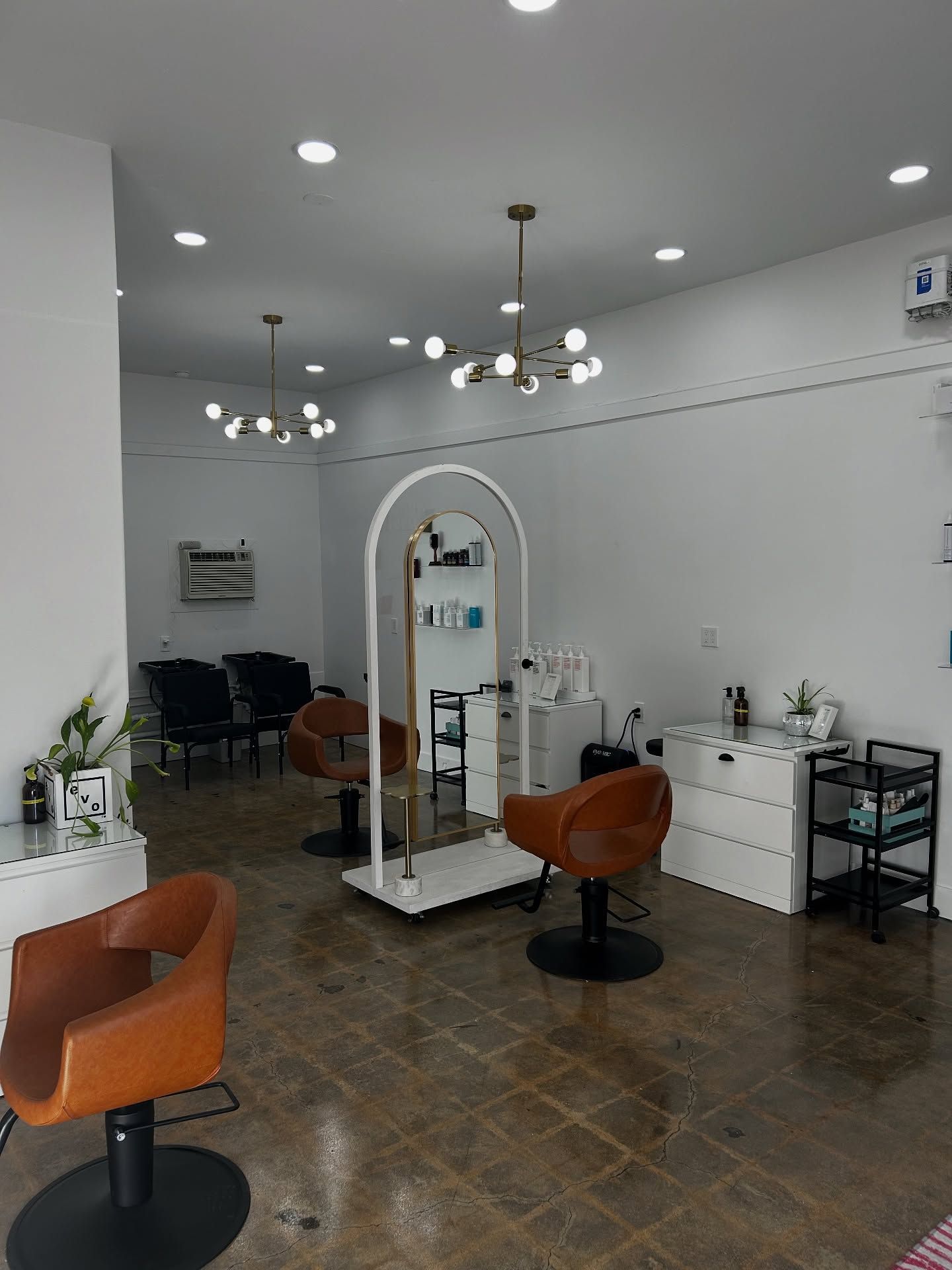 Hair salon interior with brown leather chairs, white walls, and decorative light fixtures.