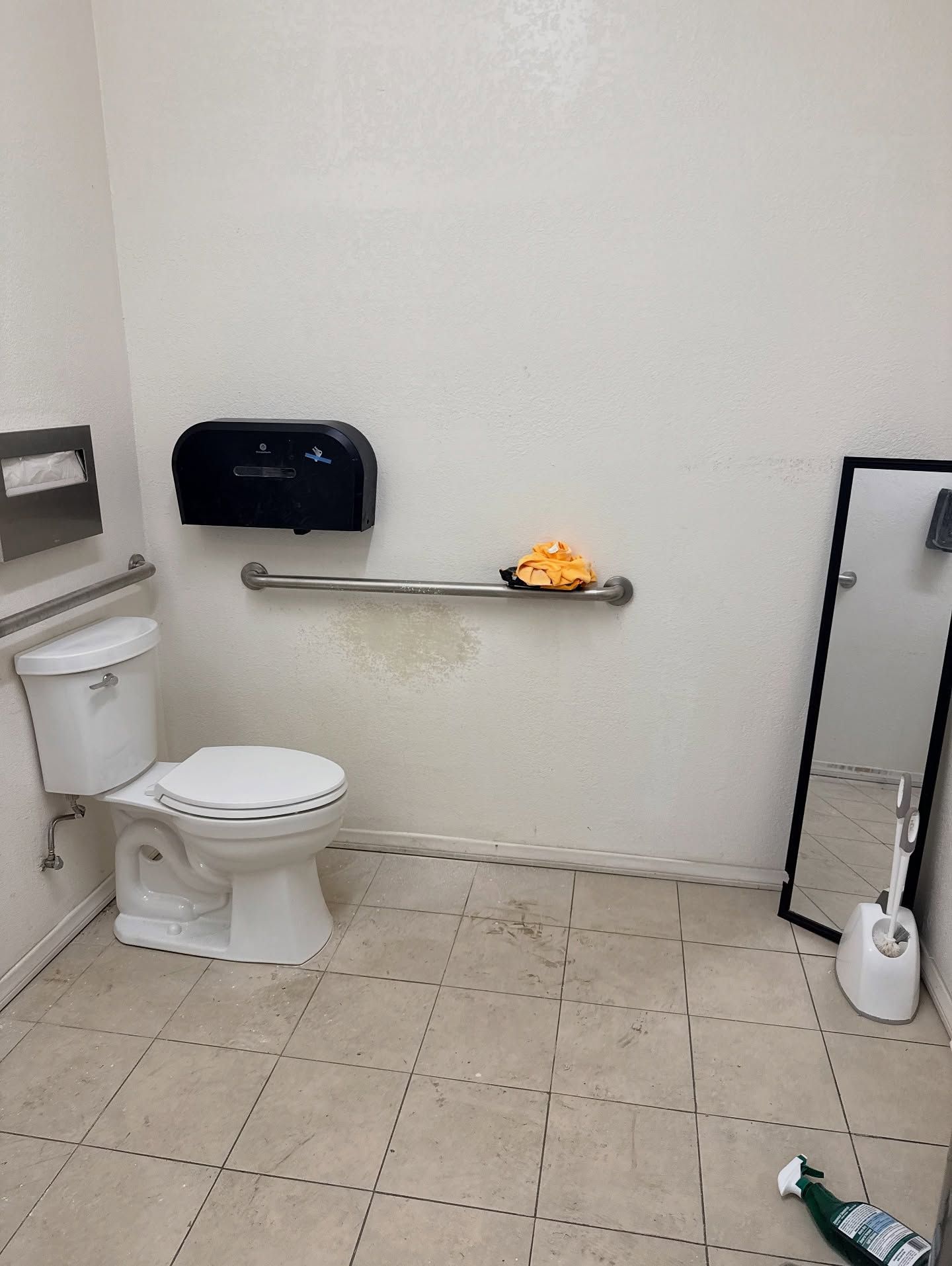 Public restroom with toilet, mirror, and handrail.