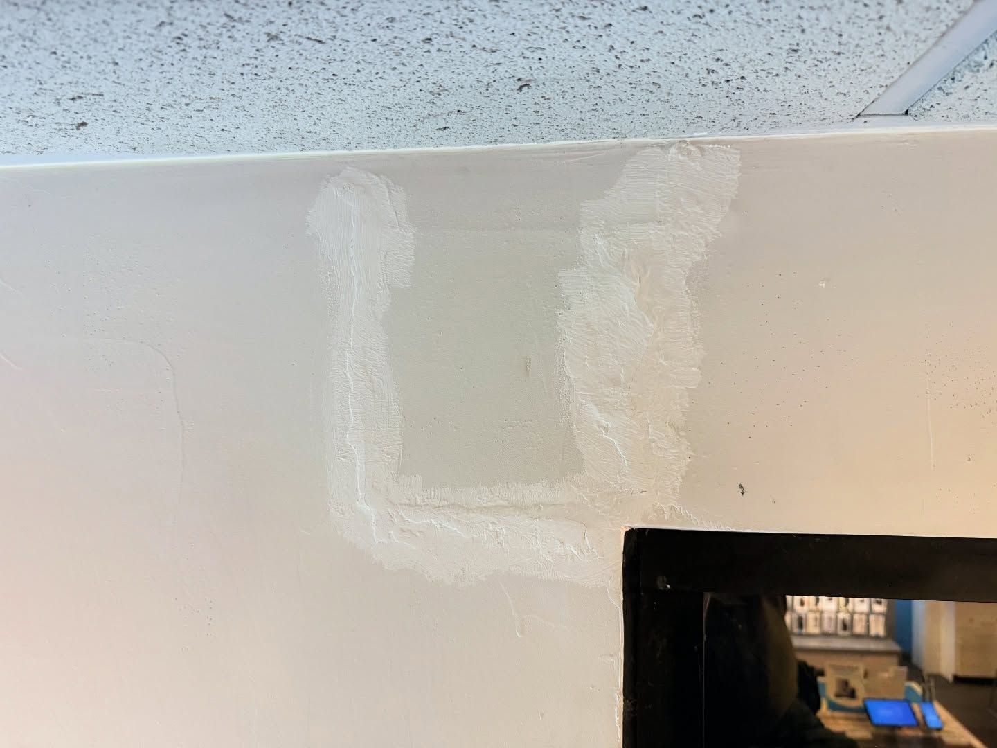 White-painted wall with a rectangular patch of lighter white material, near a black framed object.