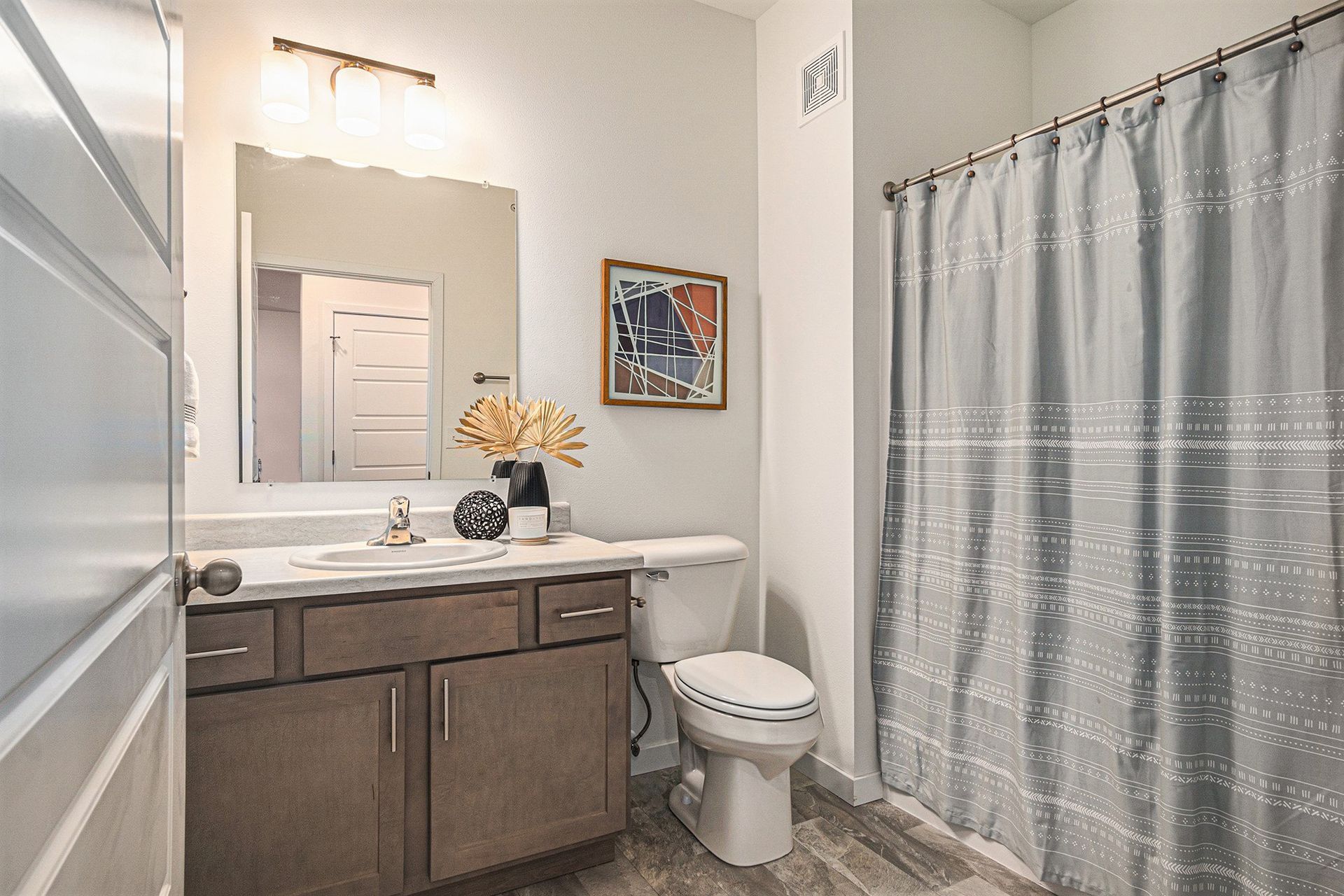 A bathroom with a toilet , sink , mirror and shower curtain.