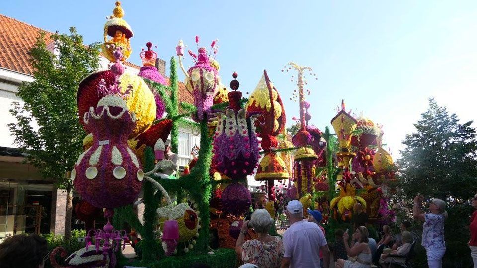 Een groep mensen loopt over straat, voor een praalwagen met bloemen erop.