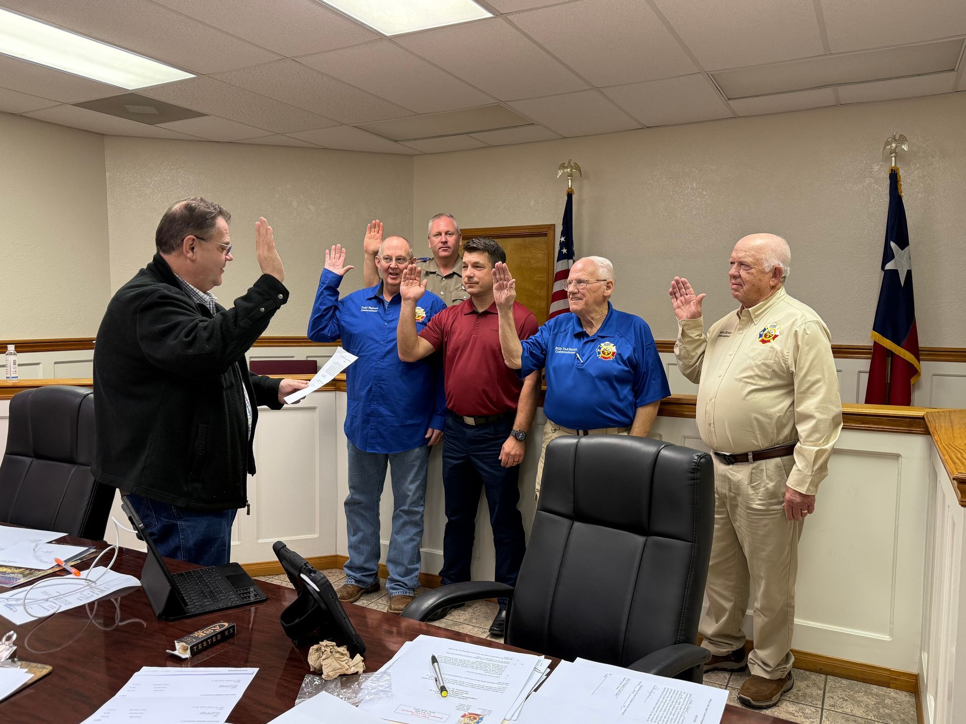 People taking oath in an office; man in front raising his hand.