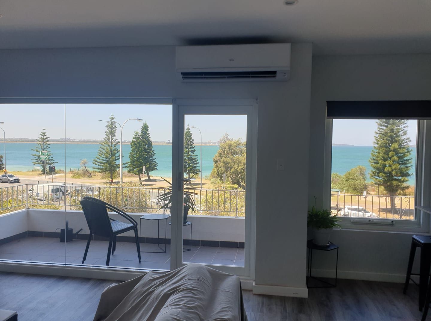 Interior view of a modern room with a balcony overlooking a body of water and a road.