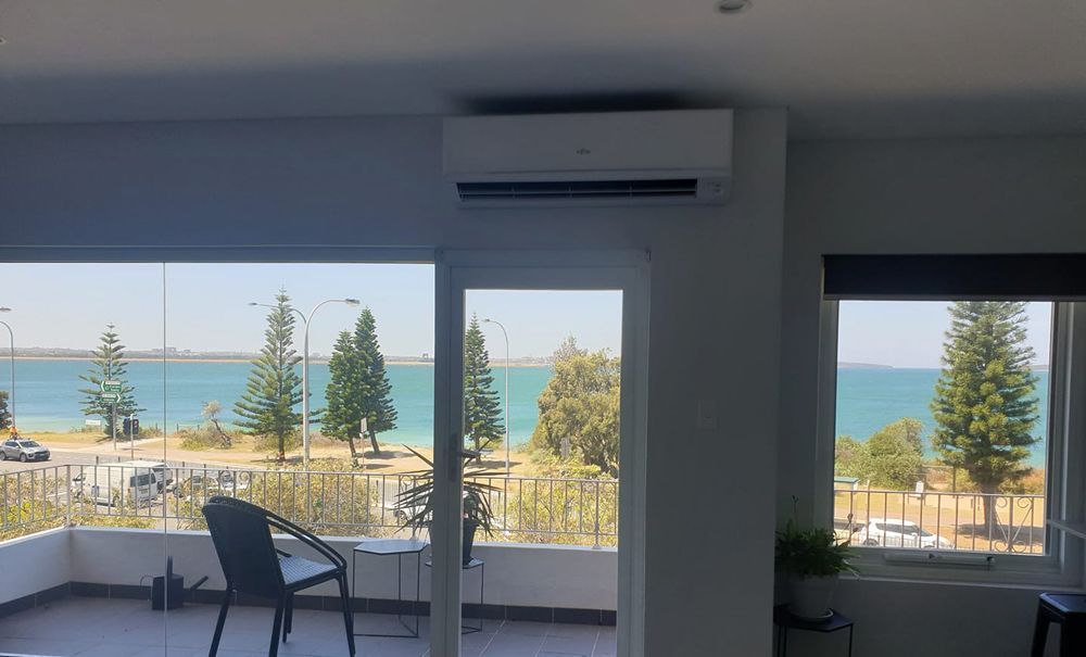 Interior with ocean view; air conditioner above window, black chair on balcony.