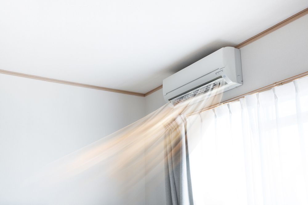 White air conditioner blows air into a room near a window.