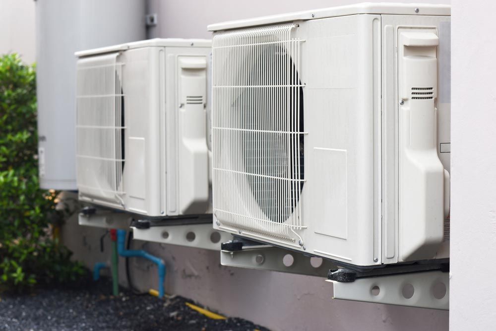 Three white air conditioning units mounted on a wall outside.