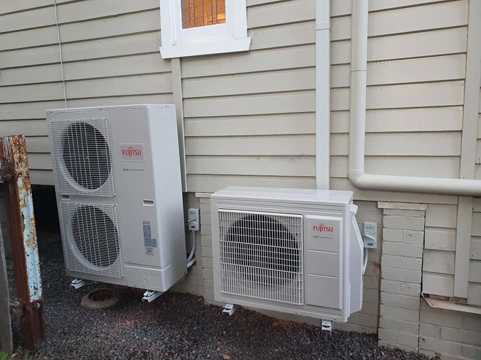 Air conditioning unit mounted on a brick wall next to a downspout and greenery.
