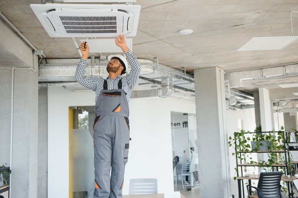 HVAC technician on a ladder, inspecting ceiling air conditioning unit in an office.