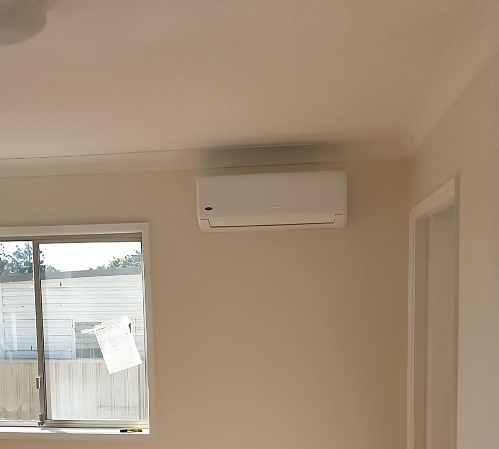 Air conditioning unit mounted on a light-colored wall, near a window and doorway.
