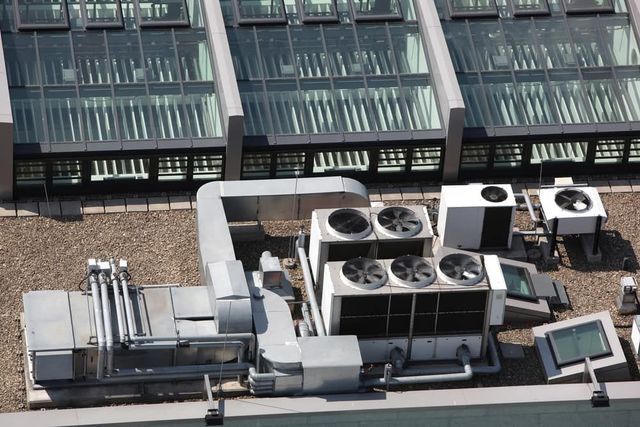 HVAC equipment on a rooftop, with multiple fans, vents, and a glass-paneled roof in the background.
