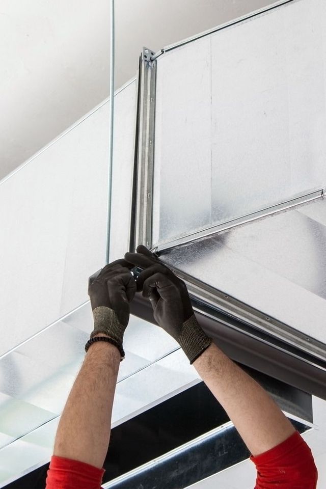 Hands in black gloves working on installing metal HVAC ductwork in a building.