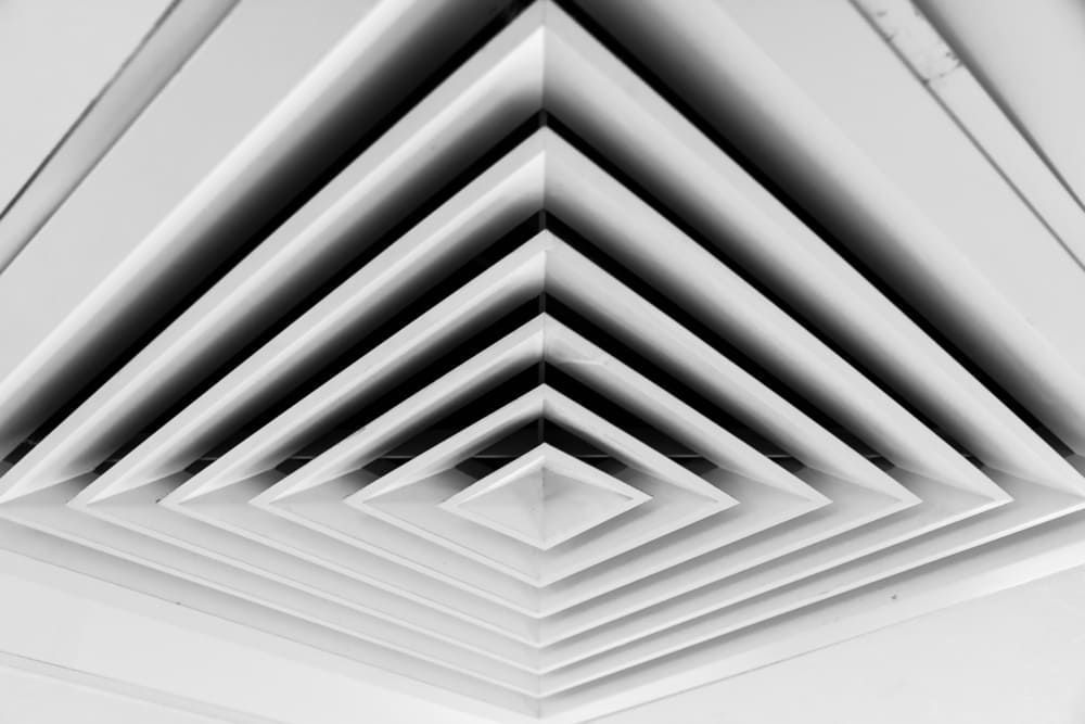 Geometric ceiling vent with layered square and diamond patterns, grayscale.
