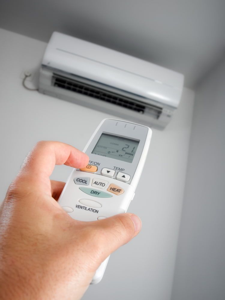 Hand holding air conditioner remote, pointing at unit on a white wall.