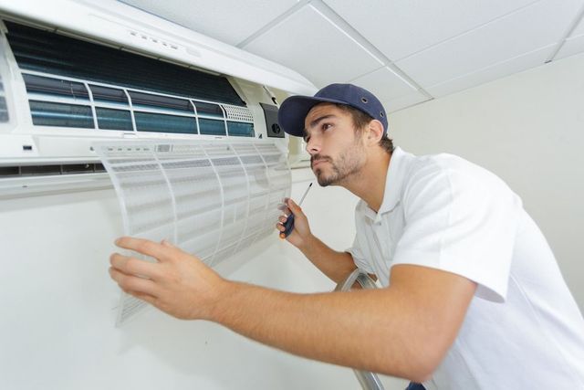 Man in cap inspecting air conditioner filter, inside.